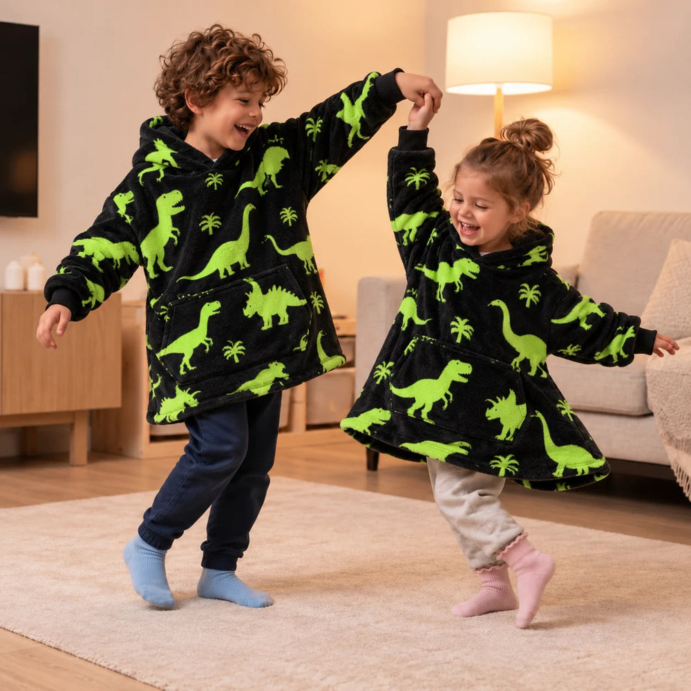 Two siblings in matching Green Dinos blanket hoodies dancing in their socks in the living room