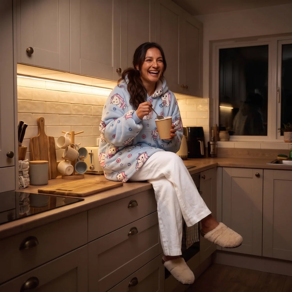 Woman wearing the Blue Unicorn blanket hoodie eating ice cream on the kitchen counter in the evening