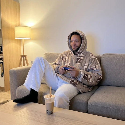 Man in the Bubble Tea blanket hoodie playing video games on the sofa, bubble tea on the coffee table