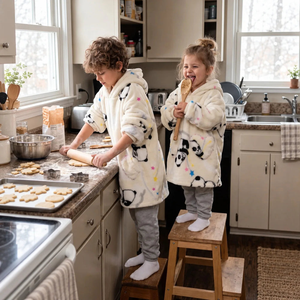 Two siblings in matching Cream Pandas blanket hoodies baking cookies in the kitchen