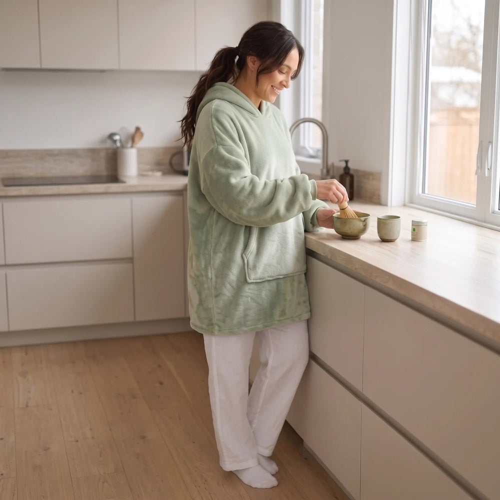 Woman wearing the Matcha Green blanket hoodie making a matcha latte in her kitchen