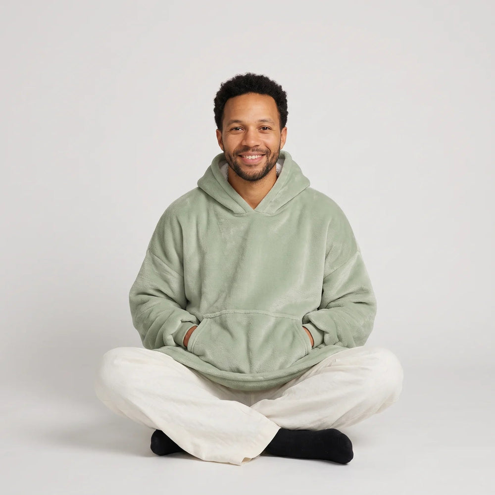 Man sitting cross-legged in the Matcha blanket hoodie, unisex fit, studio photo