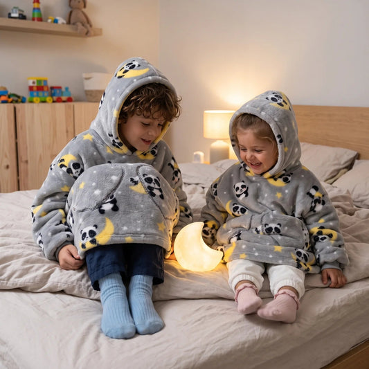 Two siblings in matching Moon Pandas blanket hoodies with a moon night light at bedtime